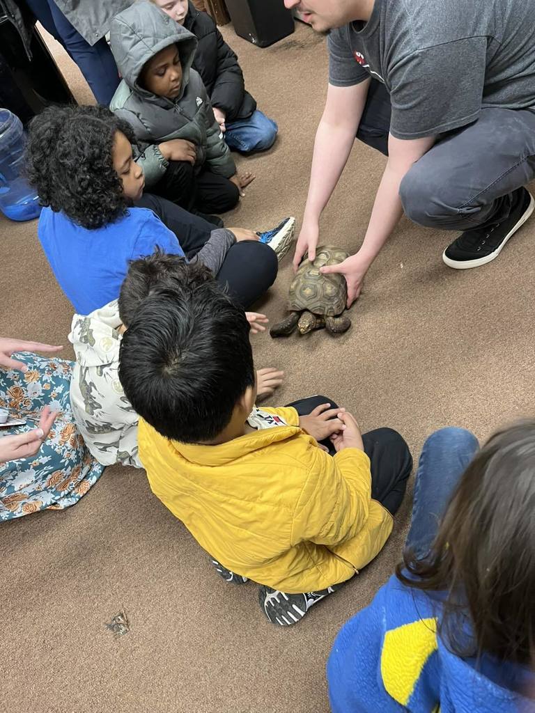 A man holding a turtle on the floor as students watch. 