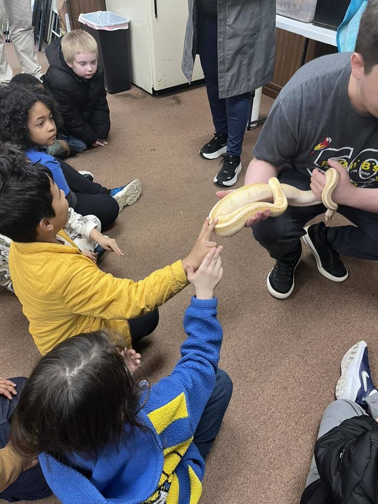 A man holding an snake as students pet it. 