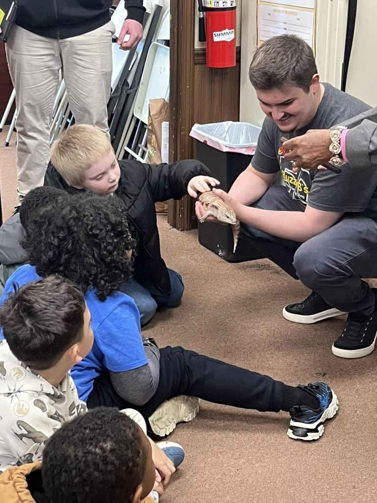 A man holding an animal as students pet it. 