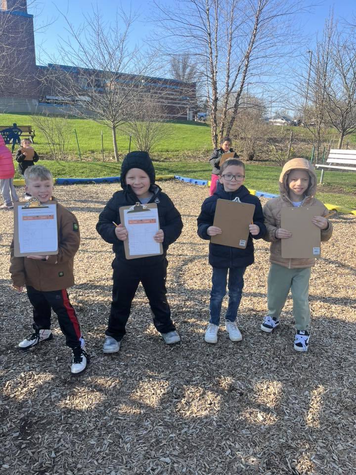 Students posing in a playground while they hold clipboards. 