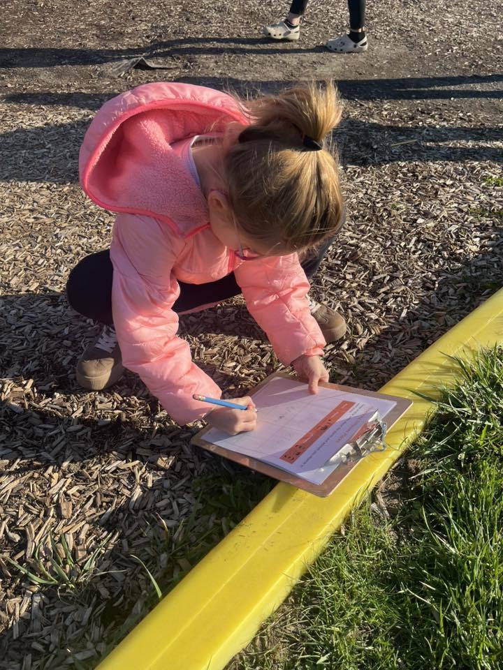 A student in a playground and is writing on a clipboard. 