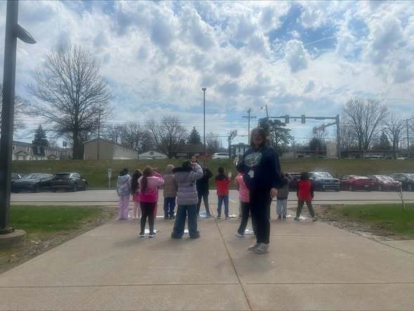 Students looking up at the sky as a teacher is standing behind them. 