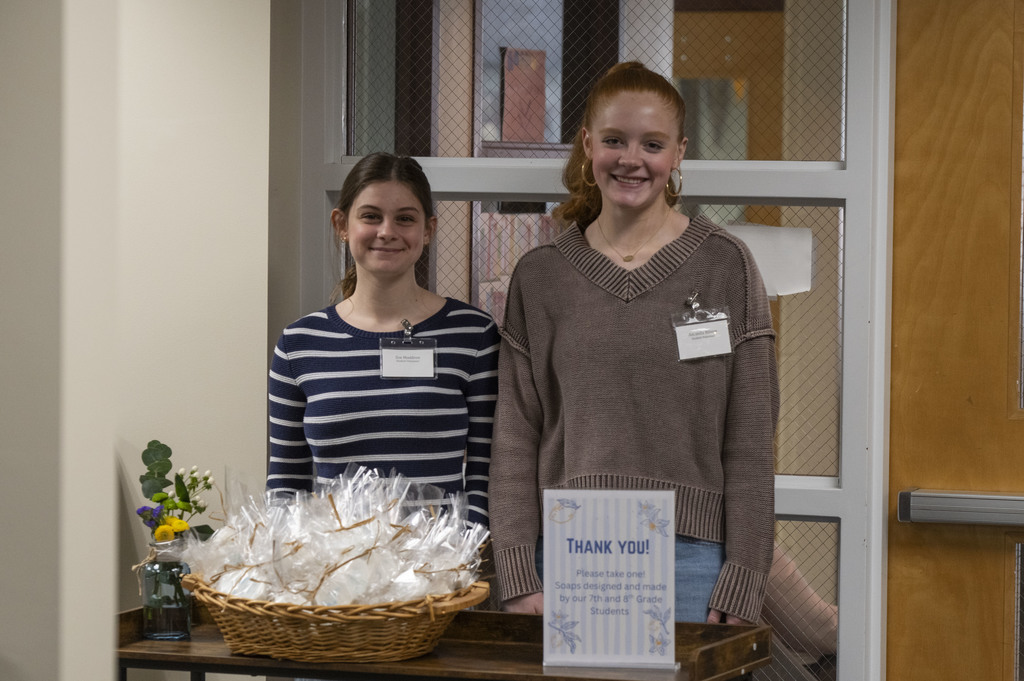 Two students, smiling, standing by  a basket of favors and a sign that says thank you.