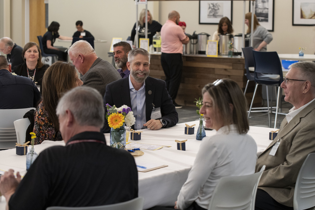 State Rep Craig Williams sits at a table with guests , smiling.