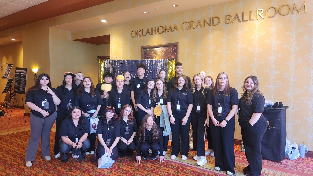 A group of people in matching black attire poses in front of an Oklahoma Grand Ballroom sign.