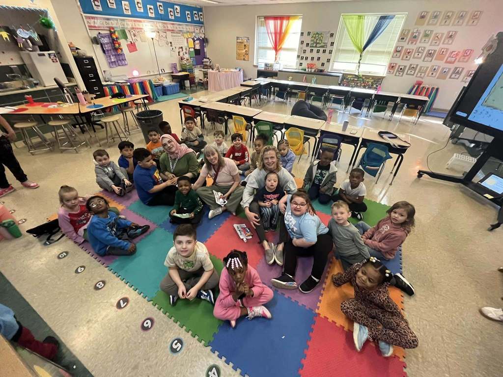 Kids and staff sitting on the floor of a colorful classroom. 