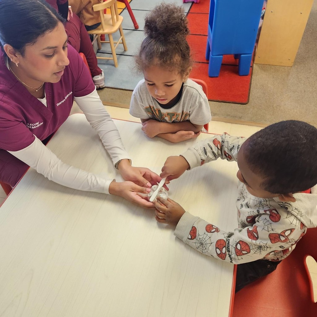 A dental student from LECOM showing two students how to brush teeth. 