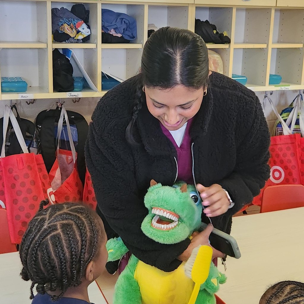A women holding a toy dragon with teeth in its mouth and showing it to a student. 