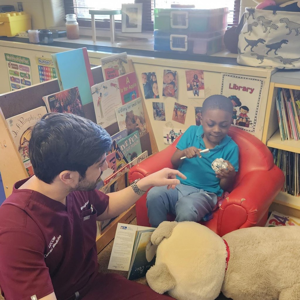A dental student from LECOM showing a student how to brush teeth. 
