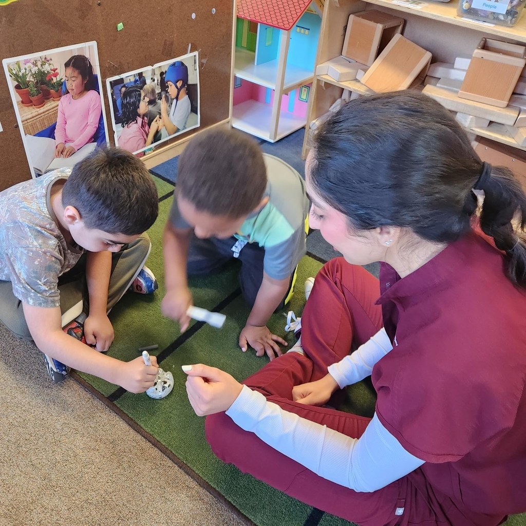 A dental student from LECOM showing two students how to brush teeth. 
