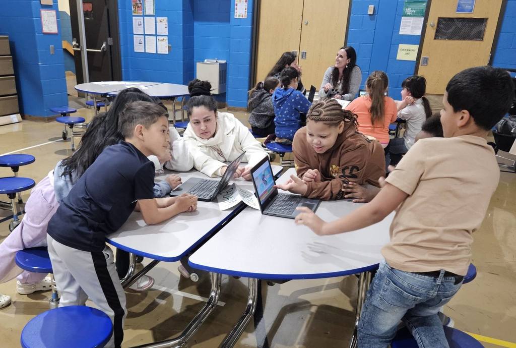 Students sitting at circle tables in school and there are computers in front of them. 