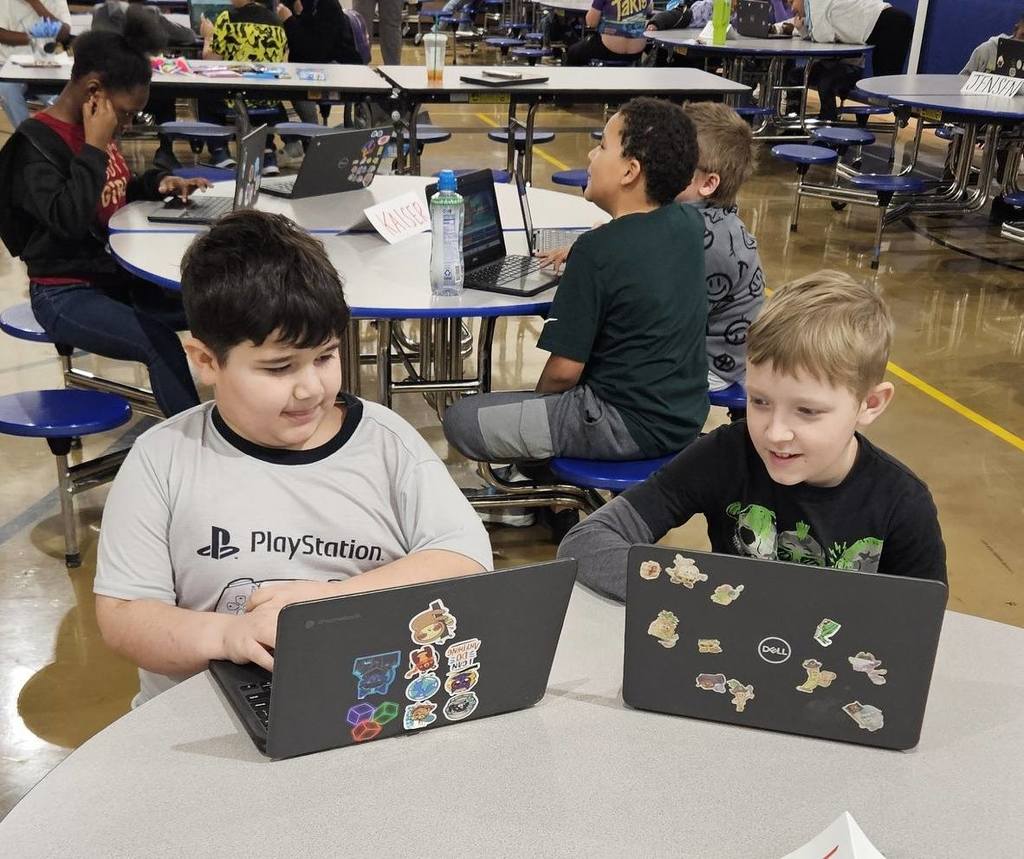 Students sitting at circle tables in school and there is a computer in front of them. 