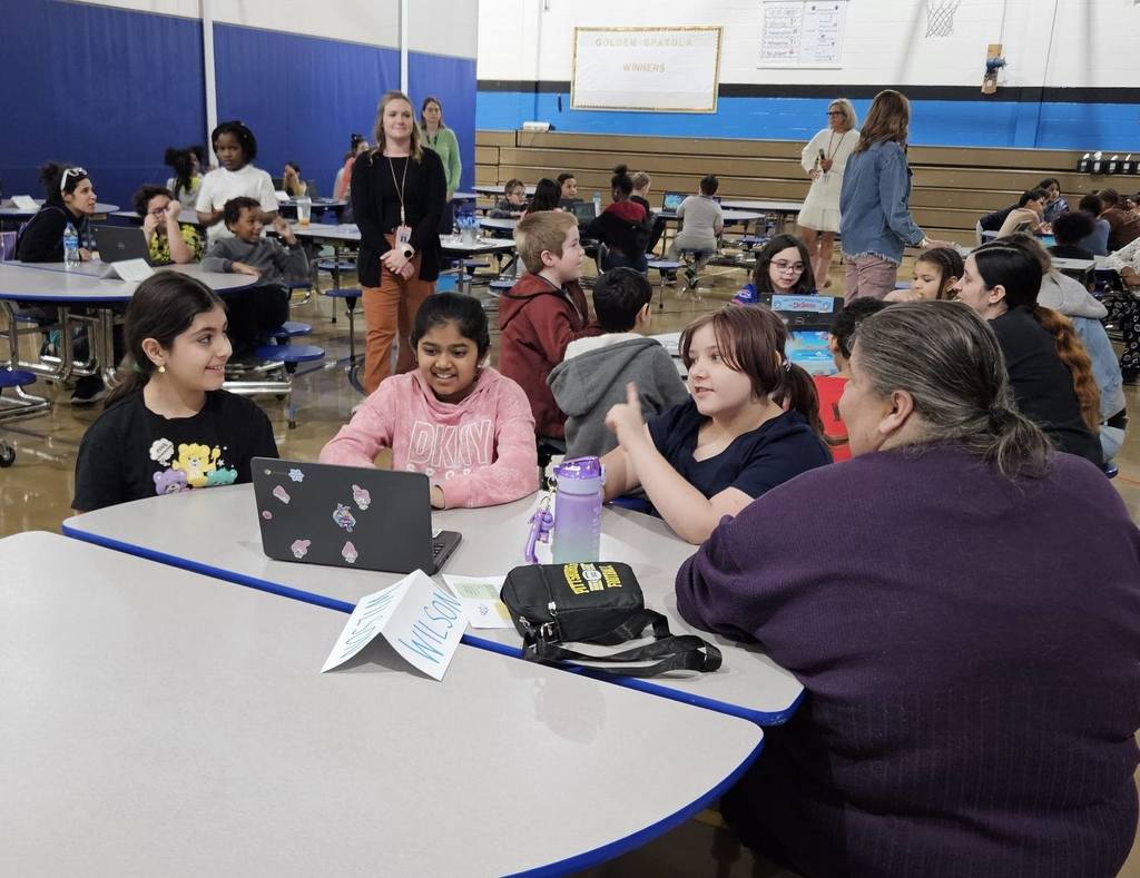Students sitting at circle tables in school and there is a computer in front of them. 
