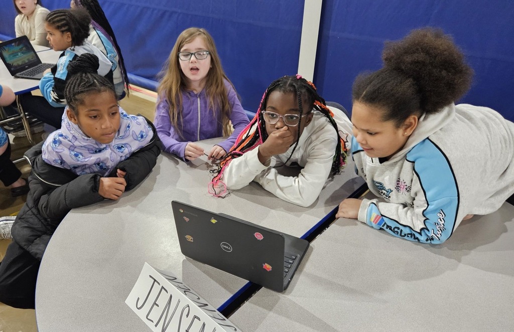 Students sitting at circle tables in school and there is a computer in front of them. 