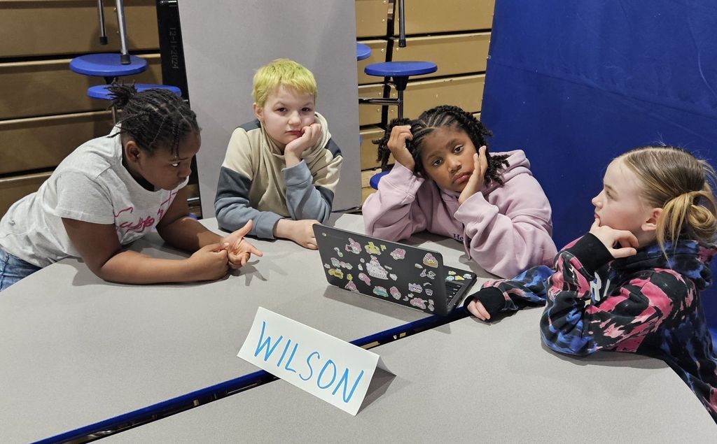 Students sitting at circle tables in school and there is a computer in front of them. 