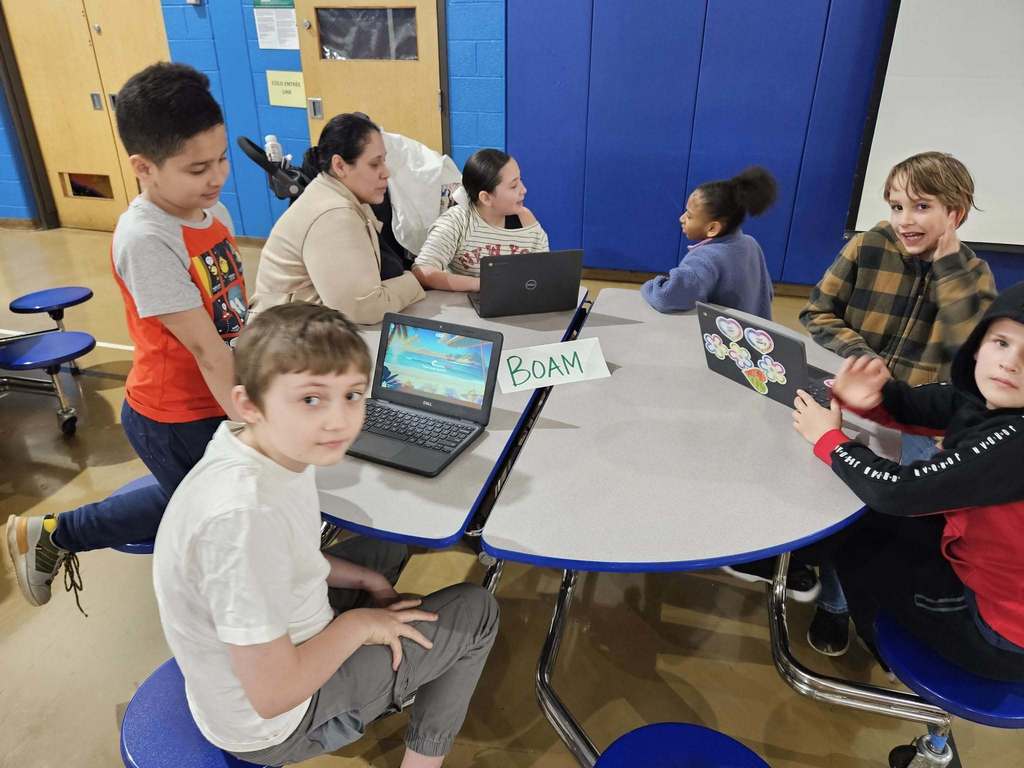 Students sitting at circle tables in school and there are computers in front of them. 