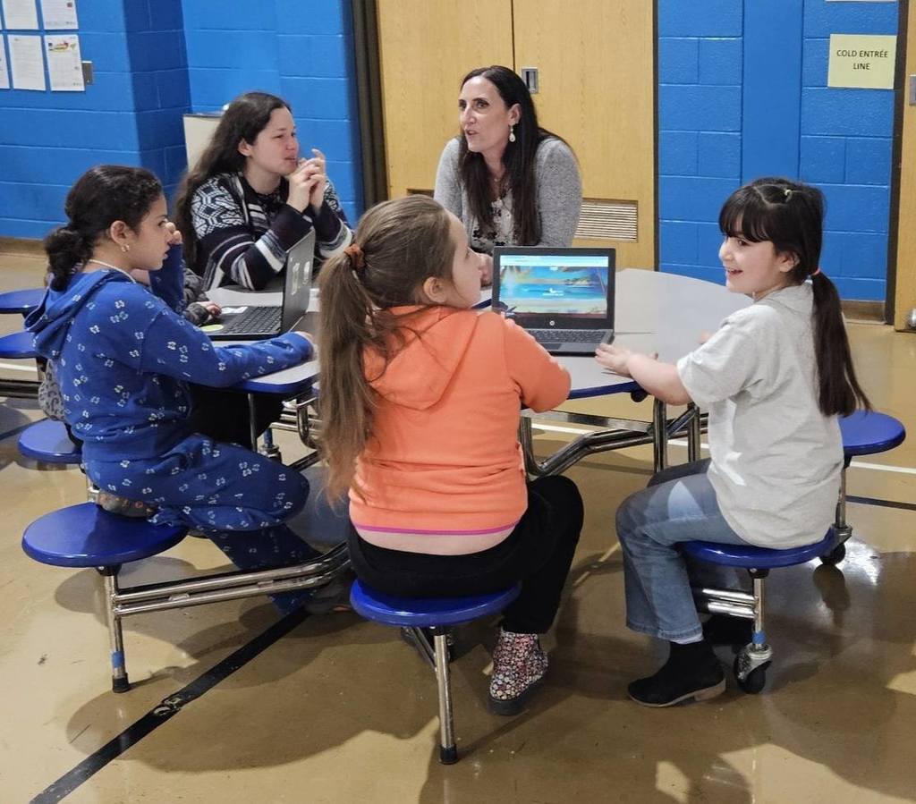 Students sitting at circle tables in school and there is a computer in front of them. 