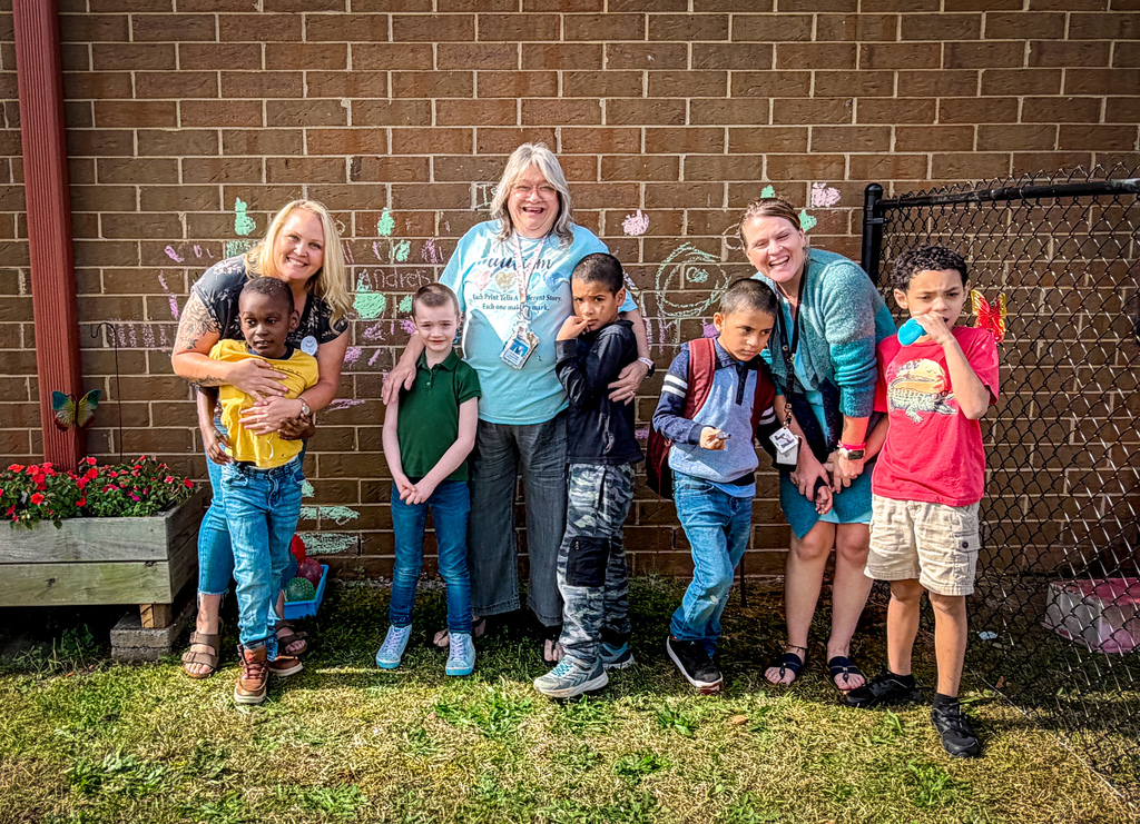 Adults and children pose for a photo, standing in a row in front of a brick wall.