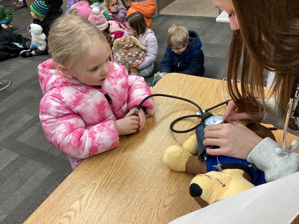 Student watches as an adult places a blood-pressure cuff on a stuffed animal during a pretend checkup.