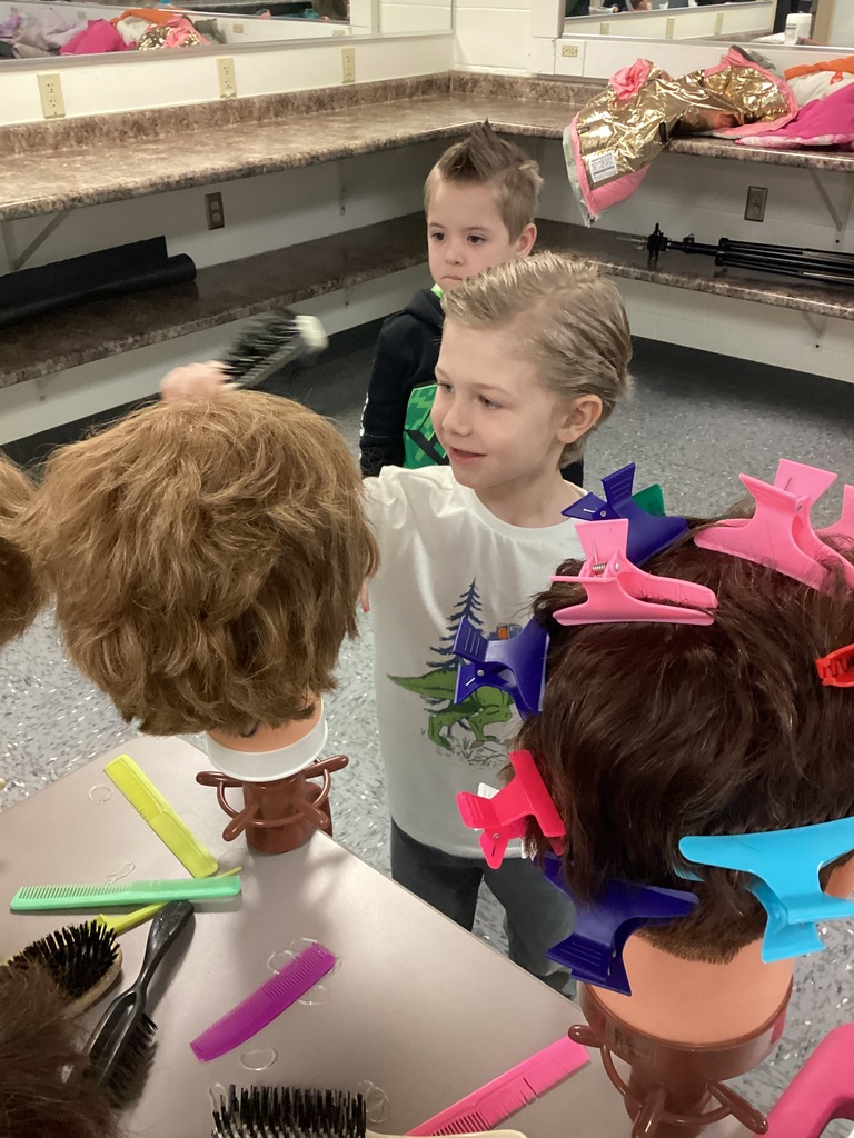 Students practice hairstyling on mannequin heads using combs, brushes, and colorful hair clips at a salon workstation.