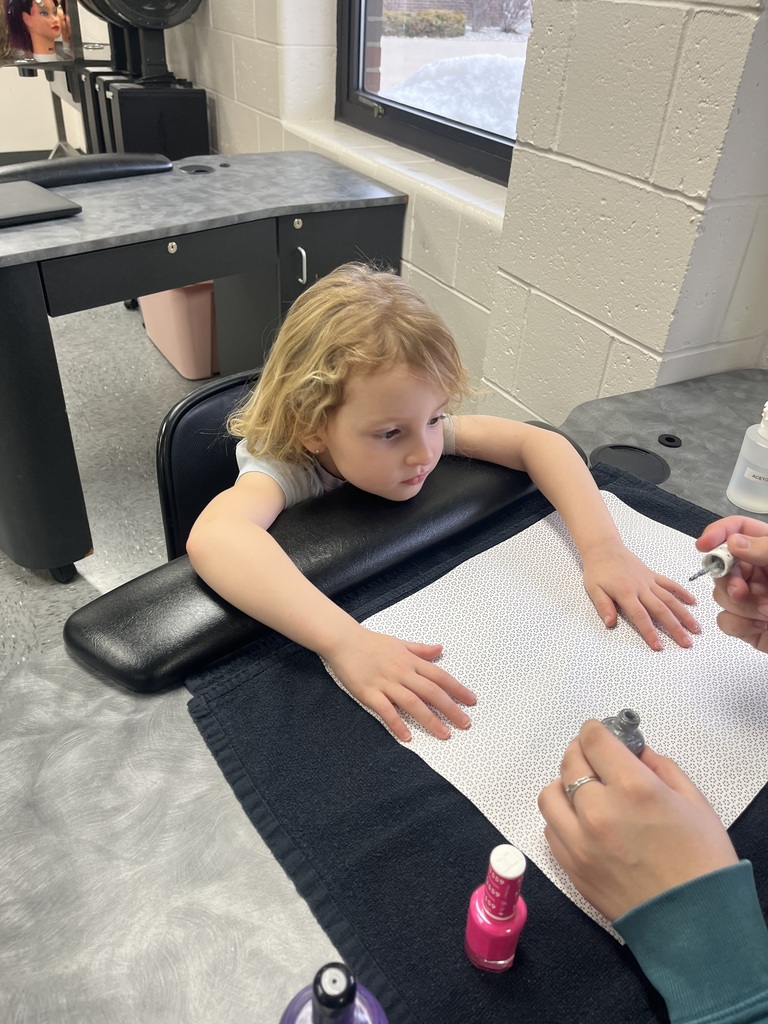 Close-up of a manicure station as an adult paints a student’s fingernails; nail polish bottles are visible on the table.