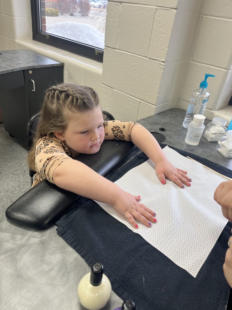 Student sits with hands on a manicure towel while an adult paints fingernails; sanitation and nail tools are on the counter