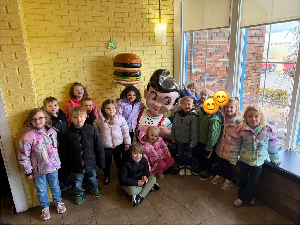 Group photo of students standing near a Big Boy statue inside a restaurant entry area with a large burger decoration on the wall.