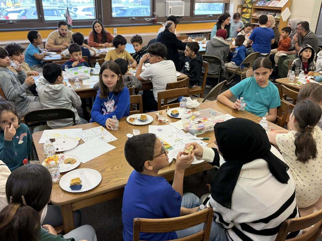 Students and adults eating at tables in school. 