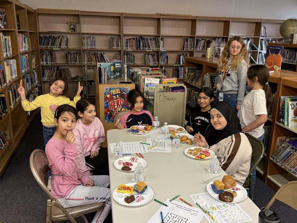 Students sitting at a table with paper and food in front of them. 