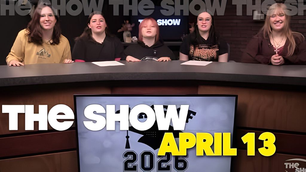 Studio set graphic showing five students seated behind a news-style desk for a student broadcast titled ‘The Show.’ A screen on the desk displays the title ‘The Show’ with the date April 13, 2026. The background includes studio lighting and a dark set design.