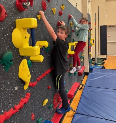 Two students climbing a rock wall