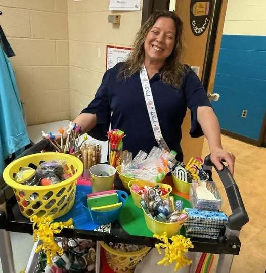 Women standing behind a card full of colorful items on it. 