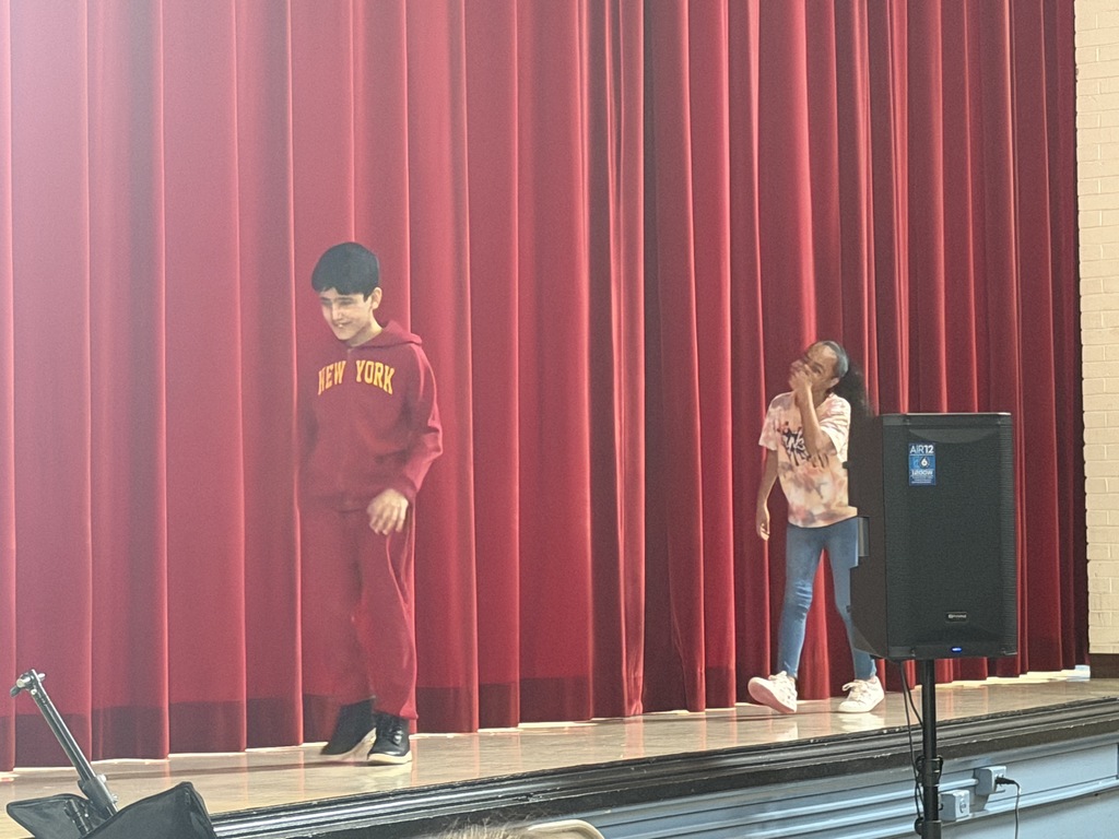 Students acting on stage while sitting. 