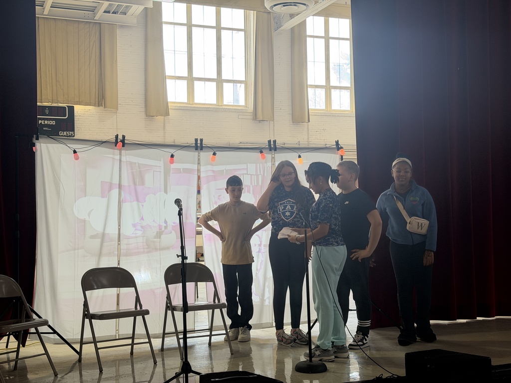 Students acting on stage while sitting. 
