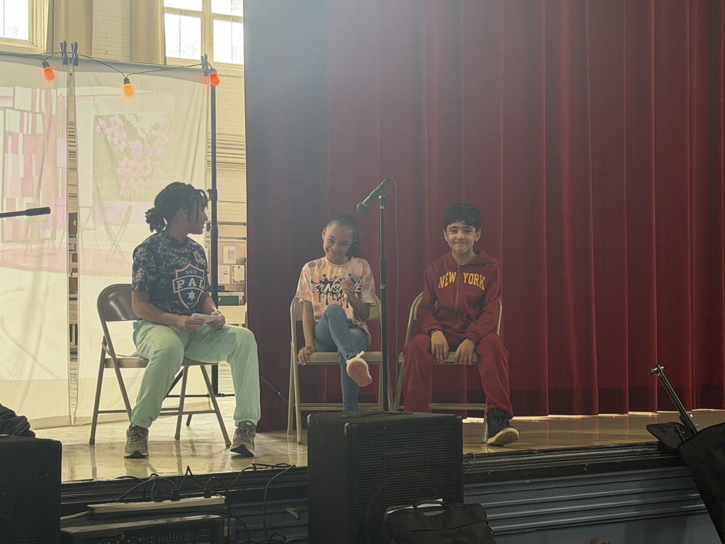 Students acting on stage while sitting. 
