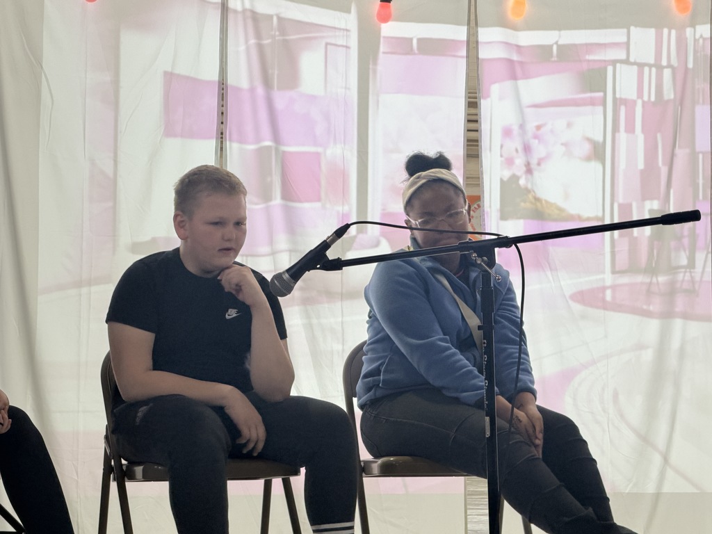 Students acting on stage while sitting. 