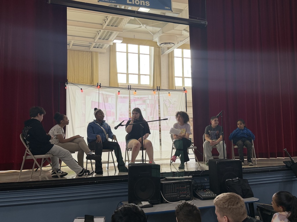 Students acting on stage while sitting. 