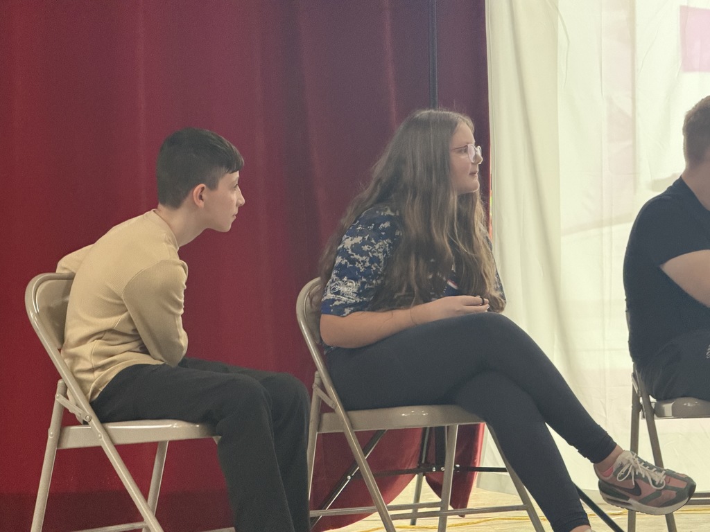 Students acting on stage while sitting. 