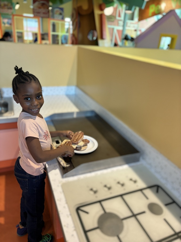 A student smiling while they play in a play kitchen. 