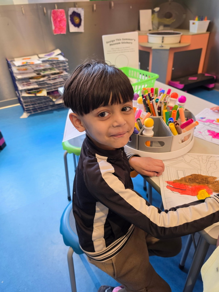 A student smiling as he colors. 