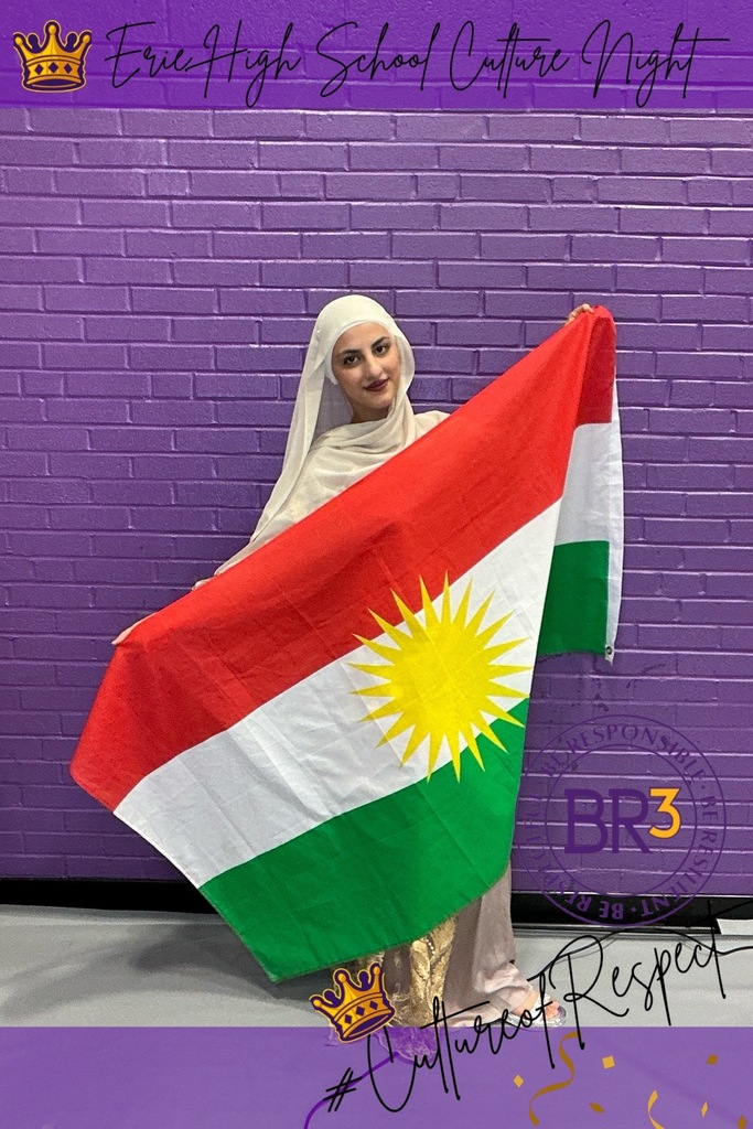 A student dressed in cultural wear and holding a flag up. 