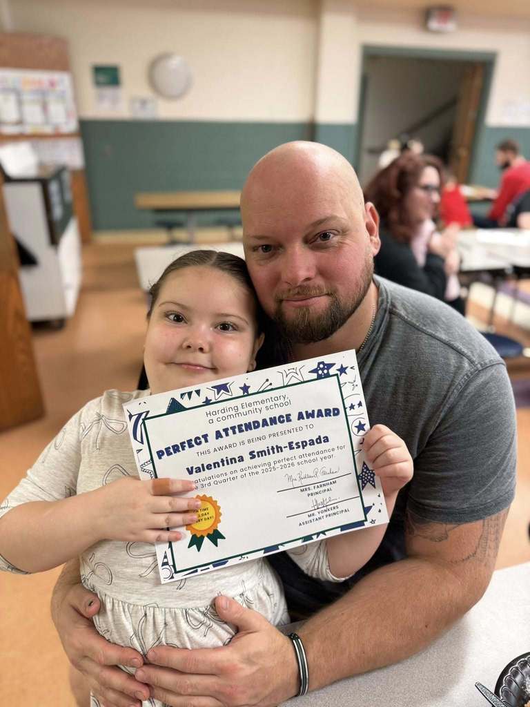 A student holding her perfect attendance award next to a man. 