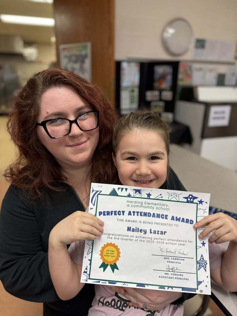 A student holding her perfect attendance award next to a woman. 