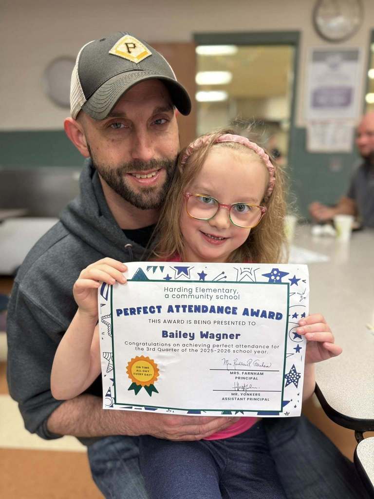 A student holding her perfect attendance award next to a man. 