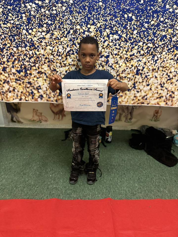 A student holding their Academic Excellence Award in front of a blue and gold backdrop.