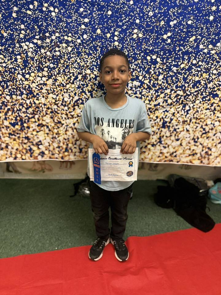A student holding their Academic Excellence Award in front of a blue and gold backdrop.