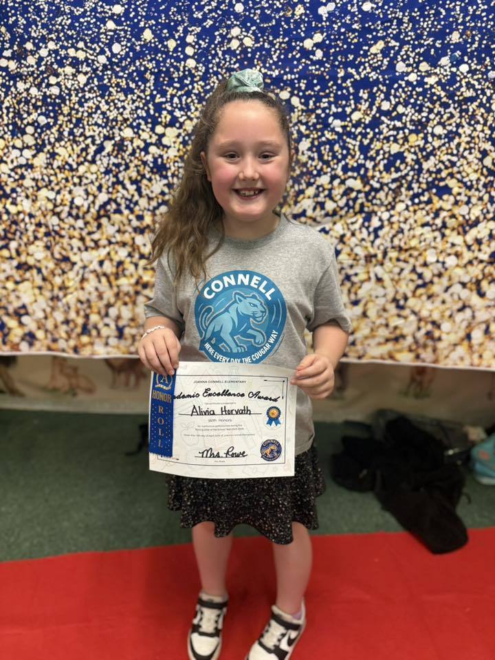 A student holding their Academic Excellence Award in front of a blue and gold backdrop.