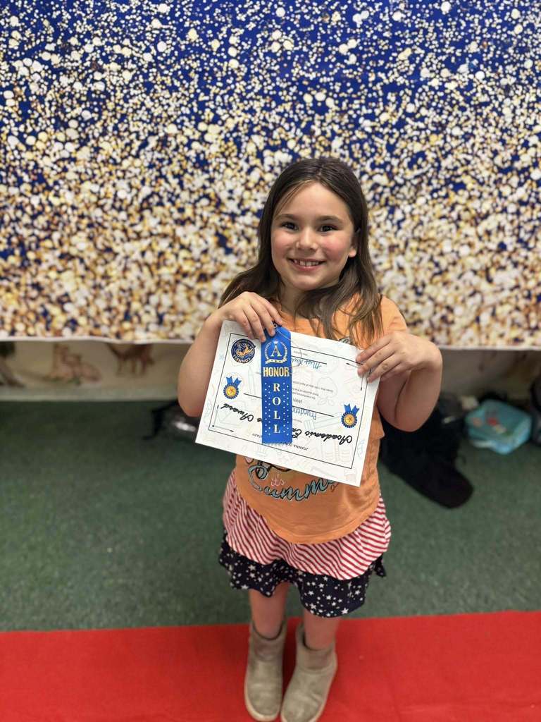 A student holding their Academic Excellence Award in front of a blue and gold backdrop.