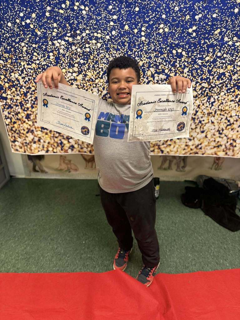A student holding two of their Academic Excellence Award in front of a blue and gold backdrop.