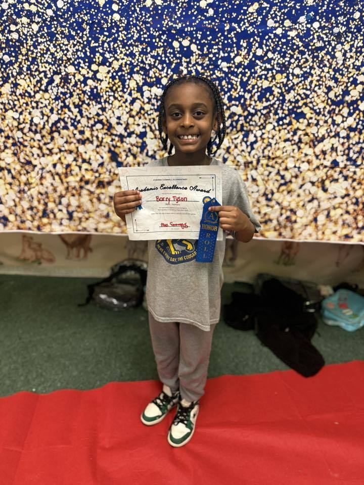 A student holding their Academic Excellence Award in front of a blue and gold backdrop.